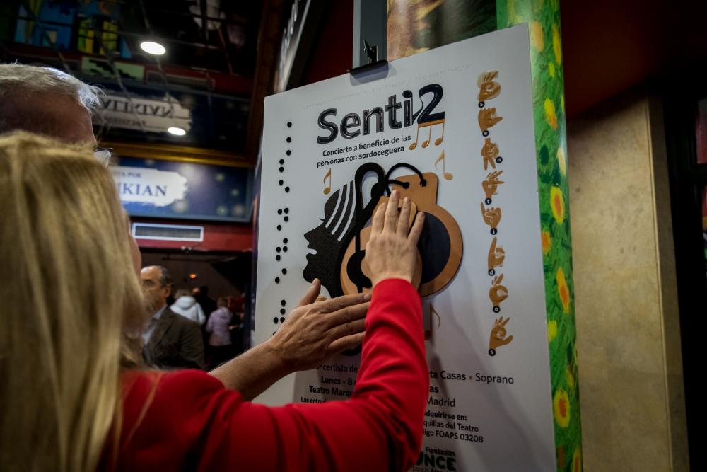 Persona con sordoceguera tocando el cartel del concierto benéfico