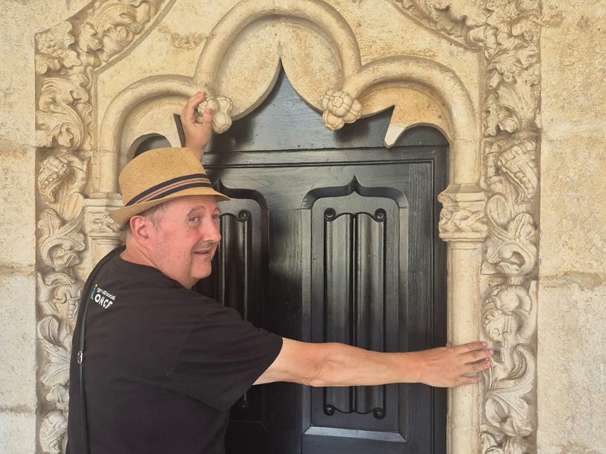 Alberto de espaldas, con una camiseta del Grupo Social ONCE, tocando una ventana de piedra tallada