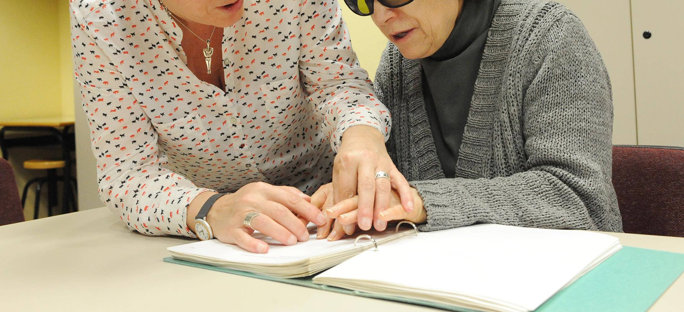 Una persona mayor con discapacidad visual leyendo con una mujer