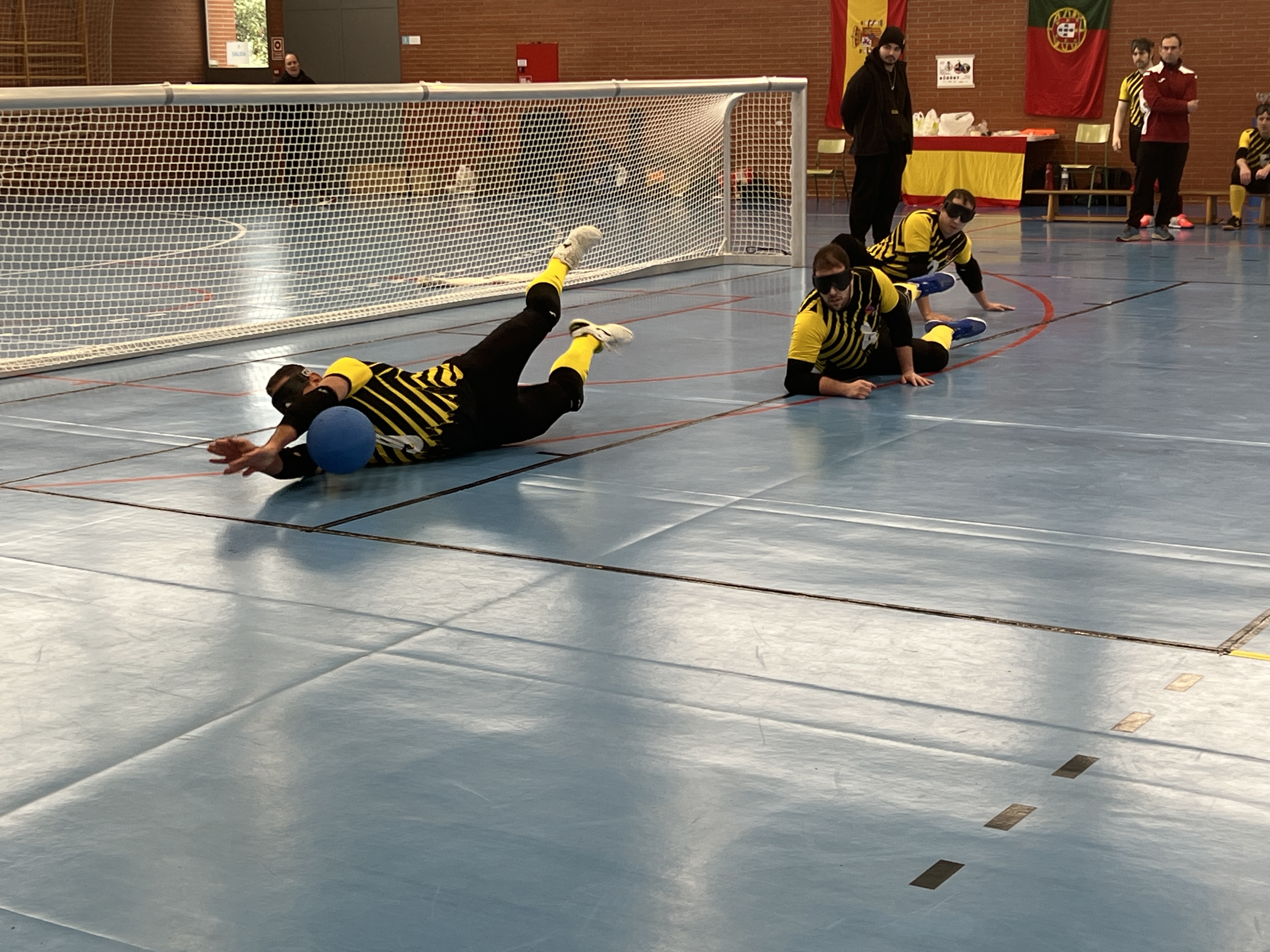 Equipo de goalball en un partido. Uno de ellos está parando el balón.