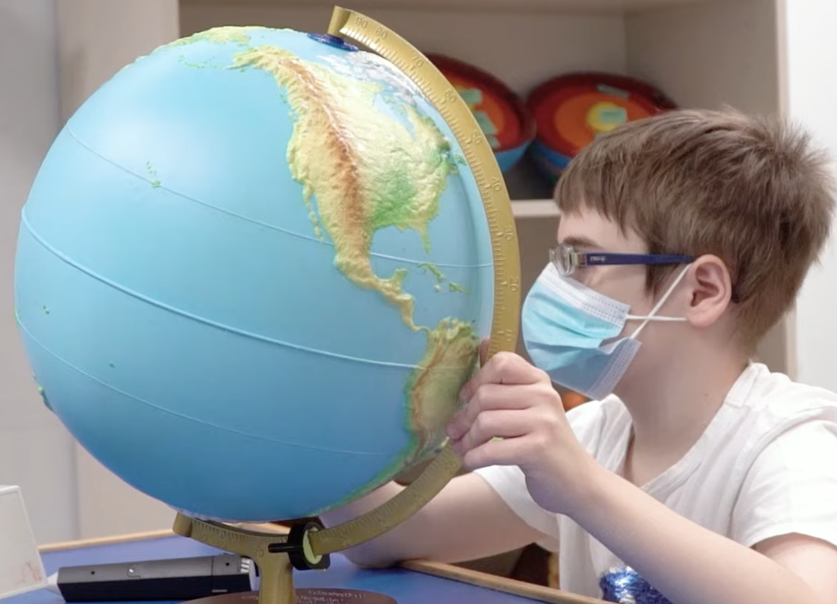 Un niño con gafas y mascarilla explora un globo terráqueo en relieve